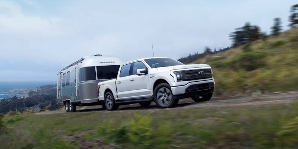 A Ford F-150 Lightning towing a trailer up a gravel road on a hillside