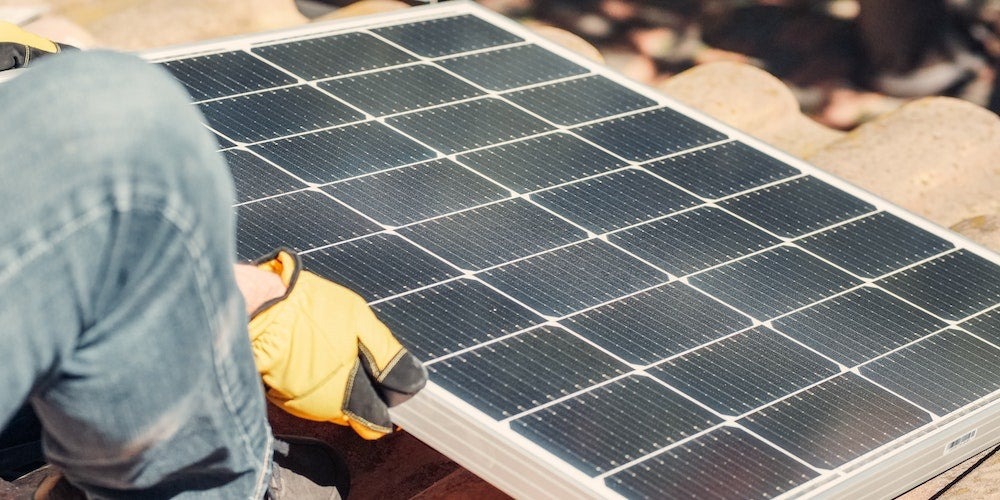 Person wearing a protective glove placing a solar panel down on a roof