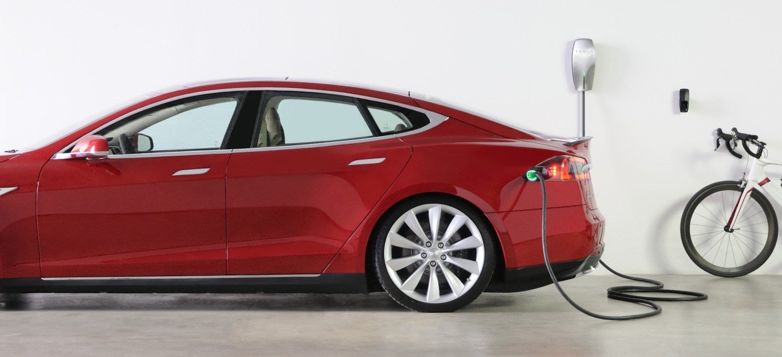 A red Tesla plugged in to a Tesla at-home charging station