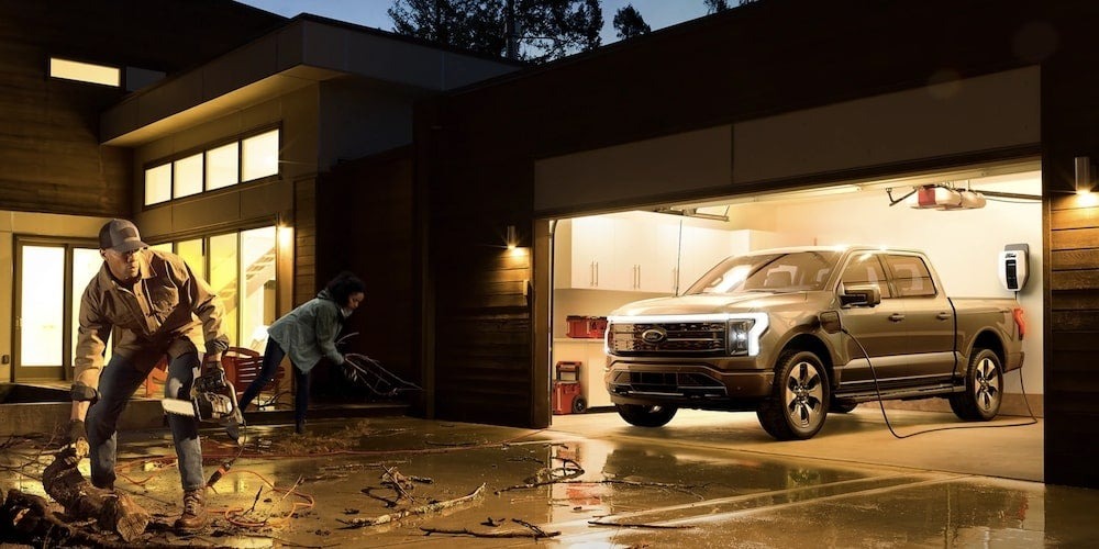 A couple picks up storm-blown debris in front of their house while their F-150 Lightning keeps the power on in the home